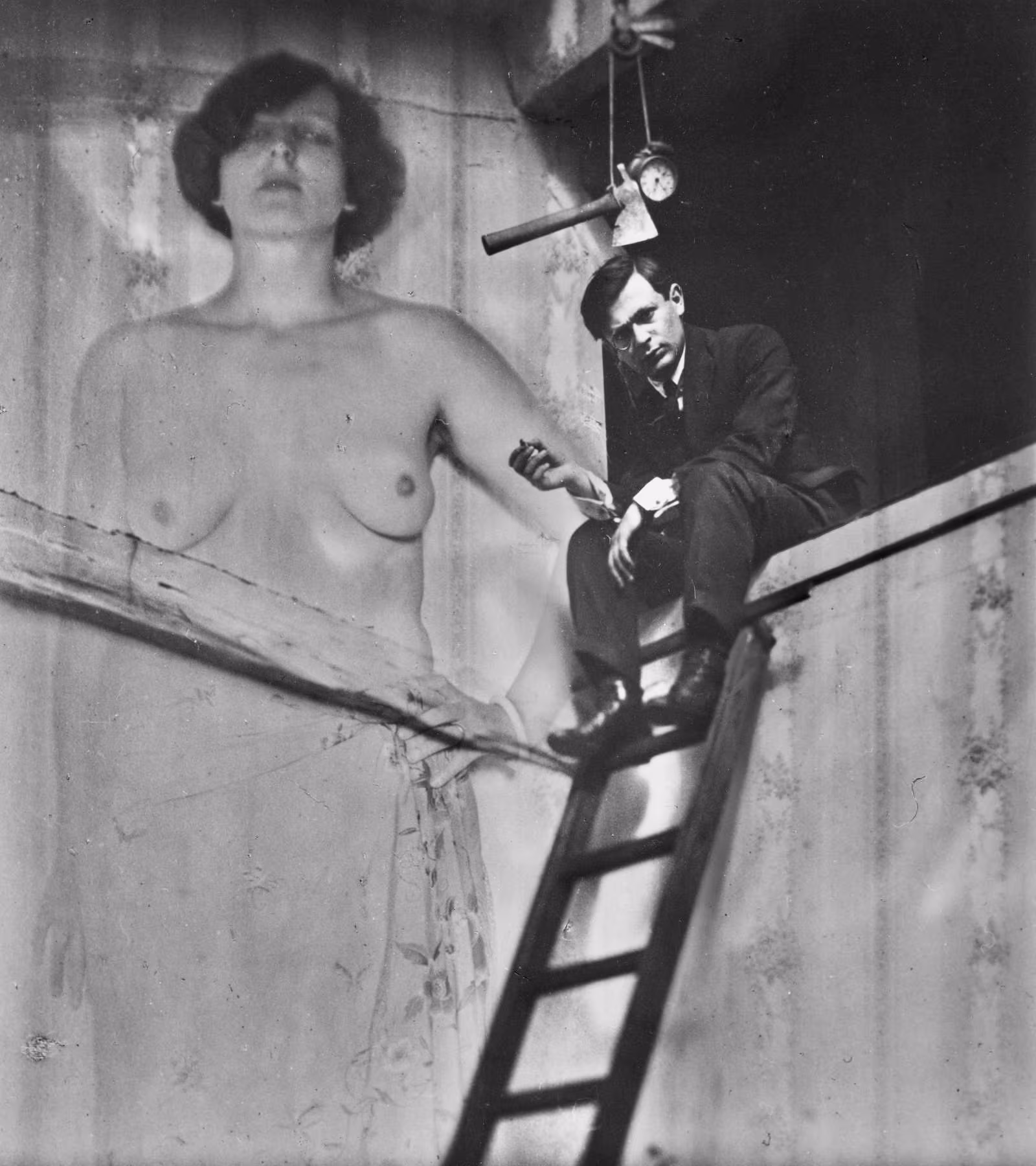 Tristan Tzara, clad in a black, three-piece suit and a white, French cuff shirt, sits in a relaxed position above a ledge, with his legs resting on the upper rungs of a ladder while holding an object in a dynamic tripod grip. Above his head hangs an axe and an alarm clock suspended by a rope. Positioned behind him and to the left is a large portrait of a bare-breasted woman's torso and face, which cuts off just below her eyes. The woman's lips are held sternly, while her arm behind Tzara is being held akimbo.